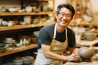 Photo of a thin middle age asian man wearingglasses, casual clothes and apron making pottery. 