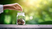 Photo of hand putting Coins in glass jar for giving and donation concept.  