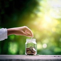 Photo of hand putting Coins in glass jar for giving and donation concept.  