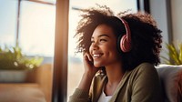 photo of A black woman sitting on a couch happy with wearing headphones in a minimal living room. 