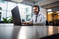 Photo of indian man working at call center, smilling talking to a laptop. 