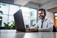 Photo of indian man working at call center, smilling talking to a laptop. 