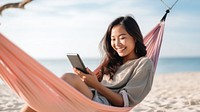 Happy traveler asian woman using mobile phone and relax in hammock on beach. 