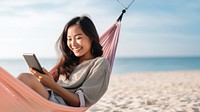 Happy traveler asian woman using mobile phone and relax in hammock on beach. 