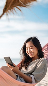 Happy traveler asian woman using mobile phone and relax in hammock on beach. AI generated Image by rawpixel.
