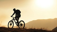 photo side view sillhuette of man riding a bicycle bike uphill with natural light. 