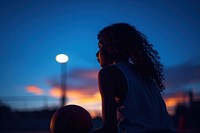 Women playing basketball, night sky. 