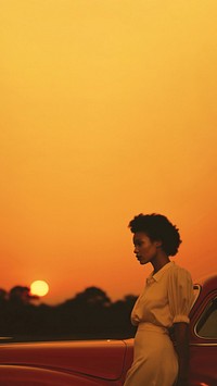 Woman standing by her car, sunset. 