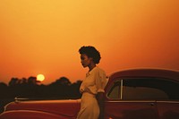 Woman standing by her car, sunset. 