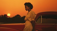 Woman standing by her car, sunset. 