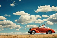 Photo of couple driving in red vintage car on countryside. 