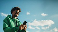 photo of black man wearing green tone outfit using smartphone. 