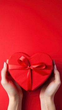 A photo of hands of woman holding a nice shape valentines present on red background.  