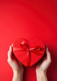 A photo of hands of woman holding a nice shape valentines present on red background.  