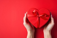 A photo of hands of woman holding a nice shape valentines present on red background.  