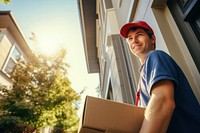 Deliveryman wearing cap holding cardboard box house architecture delivering. 