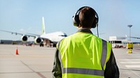 Back view photo of an airport staff wearing green safety vest and headphone.  