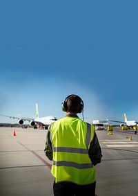 Back view photo of an airport staff wearing green safety vest and headphone.  