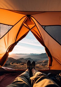 Photo of a foot of a man wearing boots stretching out of a tent, mountain view.  