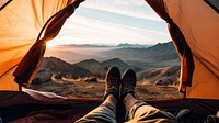 Photo of a foot of a man wearing boots stretching out of a tent, mountain view.  