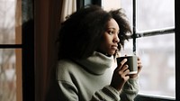 Photo of Thoughtful black woman with coffee cup looking through window in winter season.  