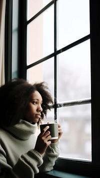 Photo of Thoughtful black woman with coffee cup looking through window in winter season.  