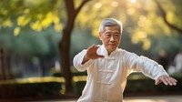 photo of an elderly asian man doing Tai chi in a park.  