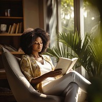 Photo of an african women wearing casual clothes reading book on an armchair, modern livingroom.  