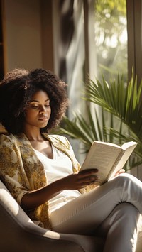 Photo of an african women wearing casual clothes reading book on an armchair, modern livingroom.  