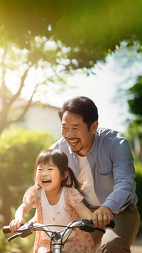 photo of an Asian father helps young daughter ride a bicycle.  