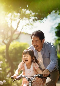 photo of an Asian father helps young daughter ride a bicycle.  