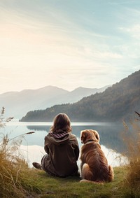 Back view photo of a hiker women sitting in a grass field with her dog looking at the lake.  