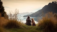 Back view photo of a hiker women sitting in a grass field with her dog looking at the lake.  