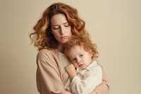 A woman with curly hair holds a young child. Both have a thoughtful expression. The child clings to the woman, creating a tender, emotional moment.