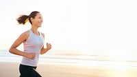 a portrait photo of a happy athletic woman jogging at sunrise by the beach.  