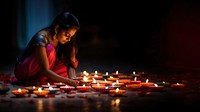 close up shot of Indian woman hand lighting diyas on Rangoli decorations on floor in Diwali festival. 