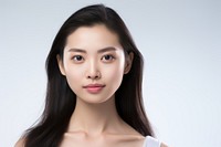 Portrait of a woman with long dark hair, wearing a white top. The woman has a calm expression. Neutral background enhances the woman's serene appearance.