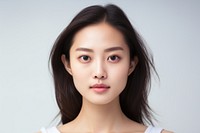 Portrait of a person with long dark hair, wearing a white top, looking directly at the camera against a light background.