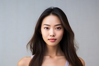 Portrait of a young woman with long dark hair, wearing a white top. She has a calm expression, standing against a neutral background.