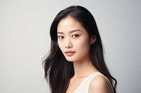 Portrait of a woman with long dark hair, wearing a white top, against a light background. She has a calm expression, looking directly at the camera.