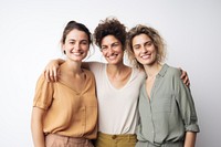 Three smiling women standing together, embracing. Casual attire, relaxed atmosphere. Neutral background, showcasing friendship and joy.