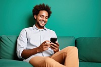 Happy young man using his cellphone while relaxing on the couch sitting portability technology. 