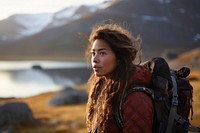 A Latina Brazilian teenage female backpacker looking at a reflective lake near a mountain in Greenland with the early morning light and mist nature outdoors hiking. AI generated Image by rawpixel.