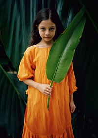 A girl wearing orange dress carry a banana leaf standing toddler adult. AI generated Image by rawpixel.