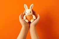 Baby hands holding fabic rabbit doll mammal orange background representation. AI generated Image by rawpixel.