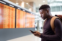 Black young man at the airport looking at the list of destinations holding a cell phone travel adult architecture. AI generated Image by rawpixel.