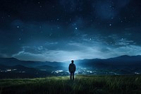 A man standing in a field by a starry night photography landscape mountain. AI generated Image by rawpixel.