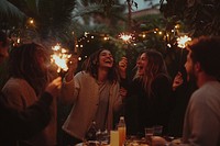 A group of friends celebrating at an outdoor garden party sparklers laughing evening.