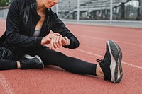 Woman warming up setting her smartwatch for tracking by stretching on a running track