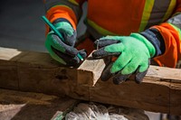 A construction worker in safety gloves measures wood before making a cut.